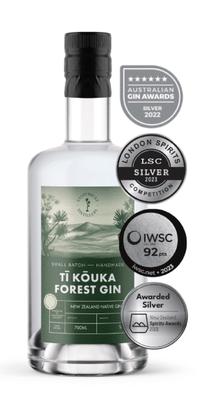 A clear glass bottle with clear liquid in it and a label on the front. The green label has illustrations of bush and a hill landscape, titled Tī Kōuka Forest Gin