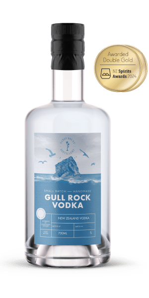 A clear glass bottle with clear liquid in it and a label on the front. The blue and white label has an illustration of a rock emerging from ocean waves, titled Gull Rock Vodka.