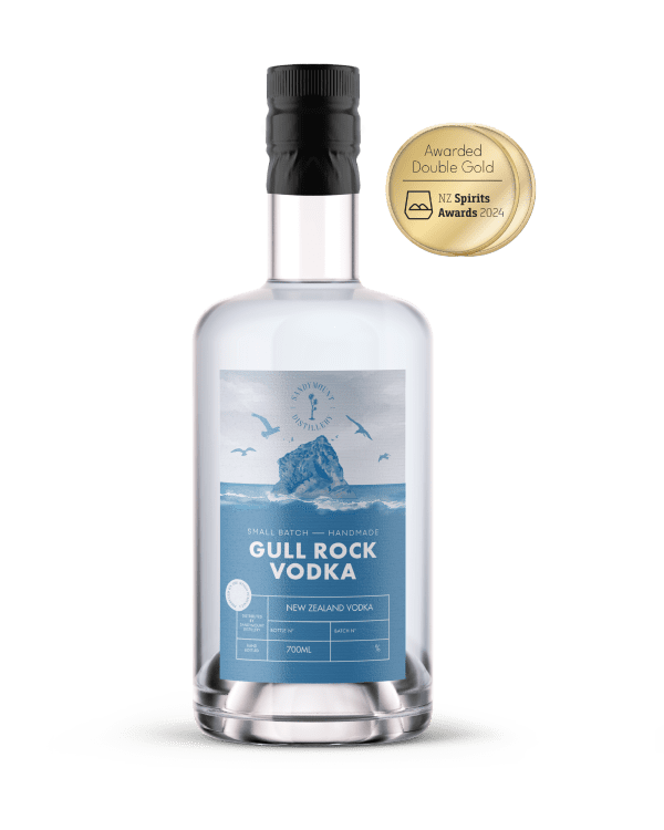 A clear glass bottle with clear liquid in it and a label on the front. The blue and white label has an illustration of a rock emerging from ocean waves, titled Gull Rock Vodka.