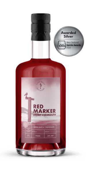 A clear glass bottle with deep red/ purple liquid (sweet vermouth). On it is a faded red label with a ship marker from the harbour, titled Red Marker.